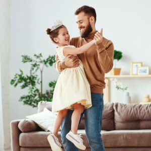 Father and young daughter dancing together in a living room