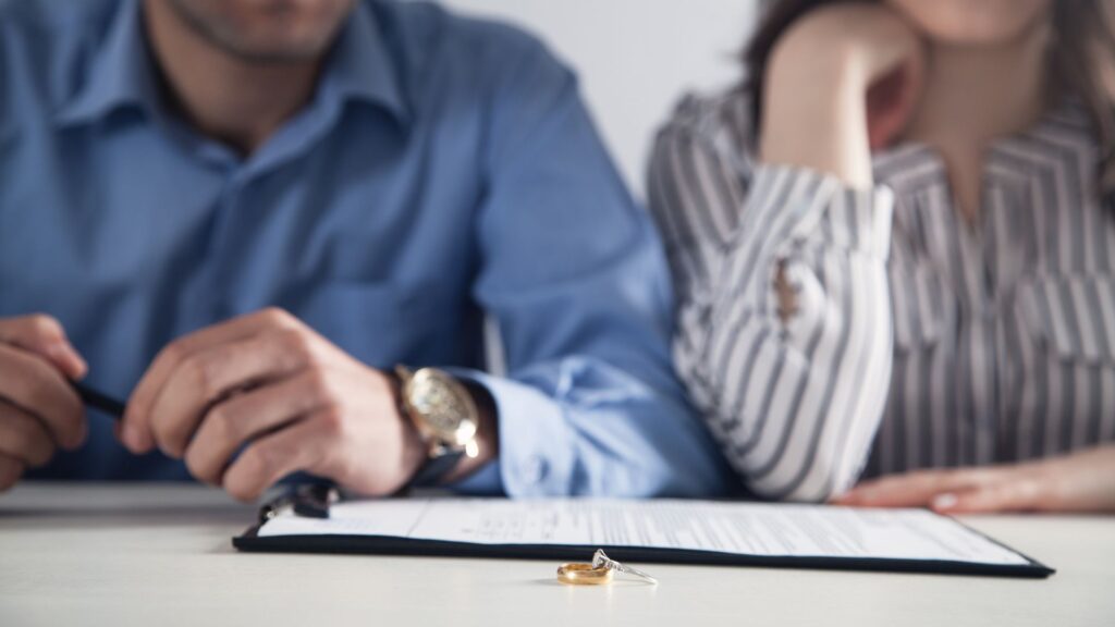 Man and a woman sitting next to each other with their wedding rings on the table in front of them.