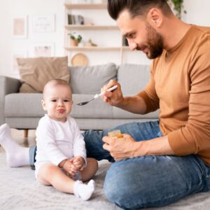 Paternity attorney in New Jersey helping father feed baby in living room