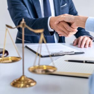 people shaking hands over paperwork in front of a scale of justice
