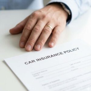 A hand rests on a car insurance policy in a naturally lit setting.