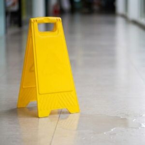 A close-up view shows a yellow caution sign on a wet tile floor in a commercial hallway.