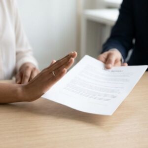 A close-up view of a hand politely pushing away a legal document in a professional office.
